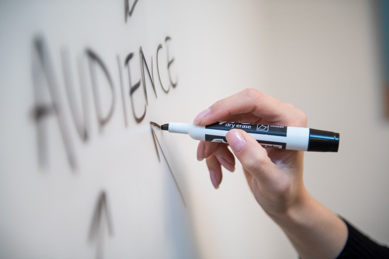A hand writing "Audience" on a whiteboard.